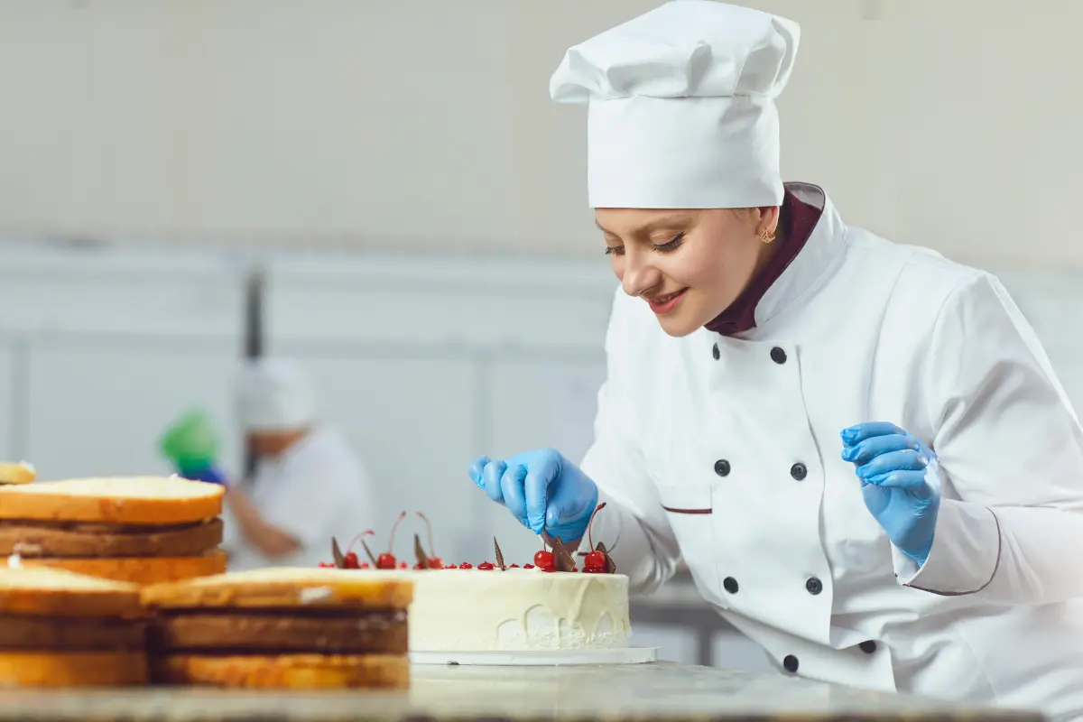 Confeiteira garantindo um acabamento impecável em um bolo artístico. Foto: Reprodução / Canva Pro.